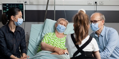 Family gathered around hospital bed wearing face masks
