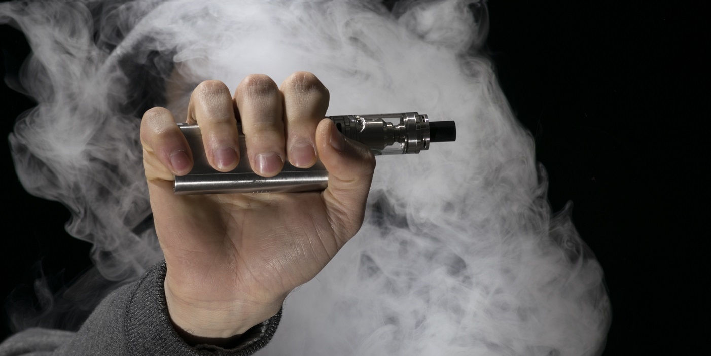 Person holding an e-cigarette or vaping device with smoke surrounding it